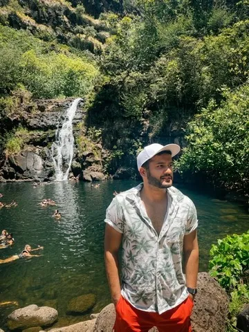 Prateek in a white cap on rocks beside a pool below a waterfall.